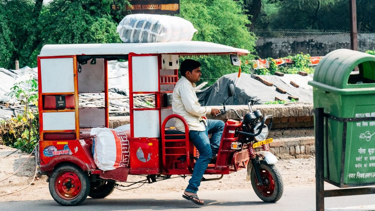 The Art of Drawing Readers In: Your attractive post title goes here A man driving a red bicycle rickshaw loaded with goods through an urban street.