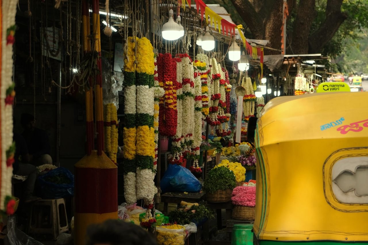 About Colorful flower market scene in Bengaluru with hanging garlands and a yellow auto rickshaw.