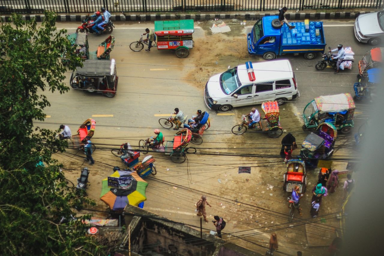 Services A vibrant aerial shot of busy street traffic in Dhaka, Bangladesh showcasing rickshaws, motorbikes, and vendors.